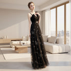 Woman in a black evening gown with floral embroidery standing on a white surface.