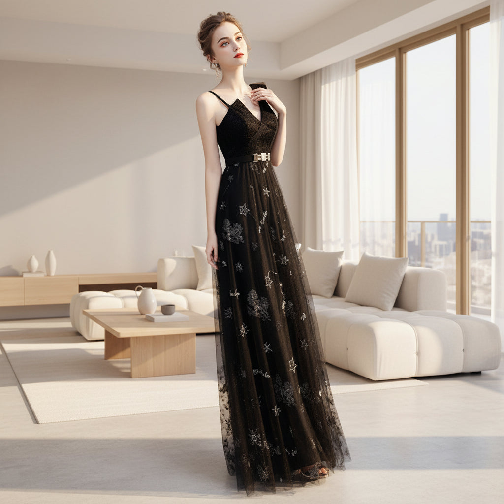Woman in a black evening gown with floral embroidery standing on a white surface.