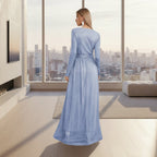 Woman wearing a long blue dress standing in a room with white walls and a small table.