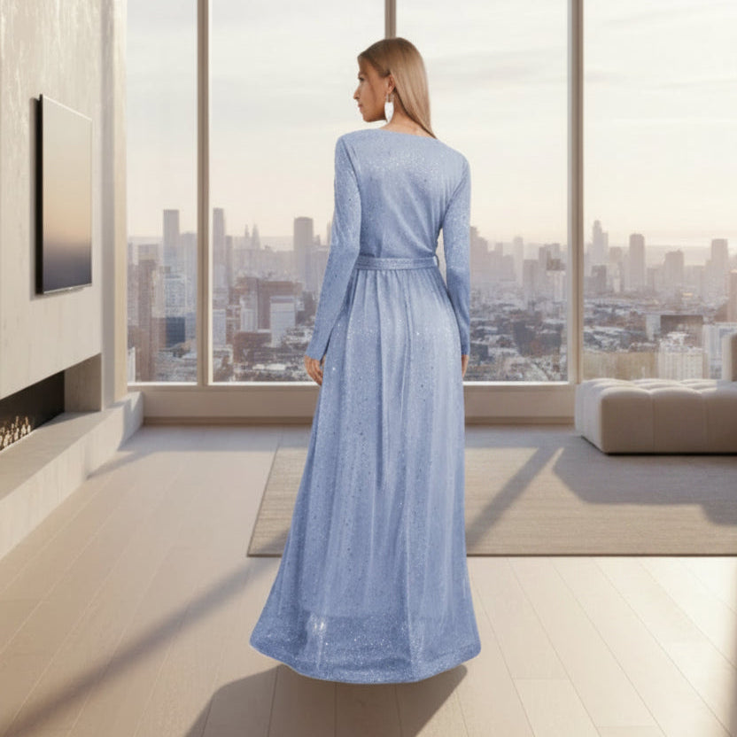 Woman wearing a long blue dress standing in a room with white walls and a small table.