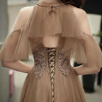 Beige evening gown with intricate detailing and sheer sleeves.
